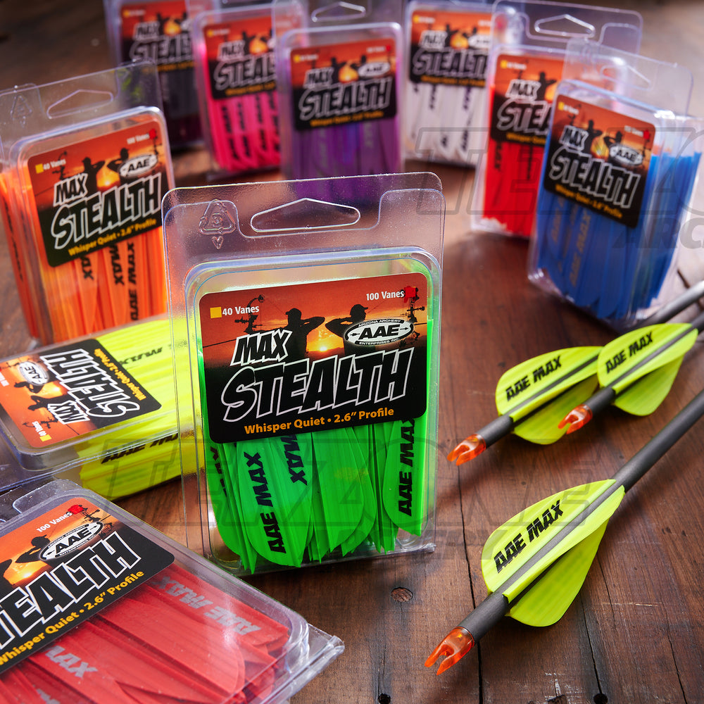 Image of ten 40-packs of AAE Max Stealth 2.6 inch vanes, each pack containing a different colour, on a timber surface with three arrows fletched with yellow Max Stealth vanes. The Ten Zone Archery logo is visible as a watermark over the image.